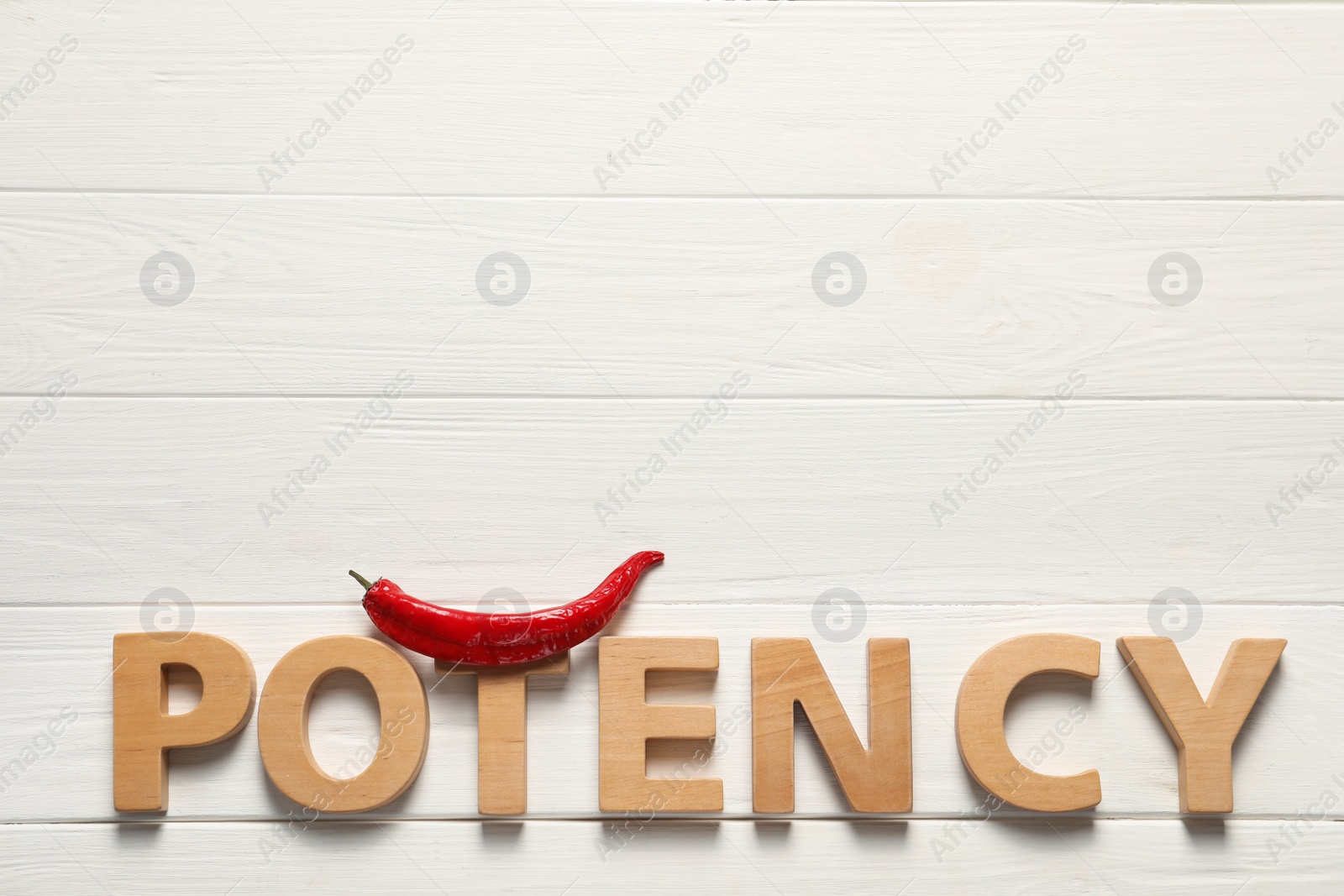 Photo of Word Potency made of letters and chili pepper on white wooden table, flat lay. Space for text