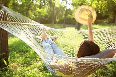 Photo of Young woman with hat resting in comfortable hammock at green garden