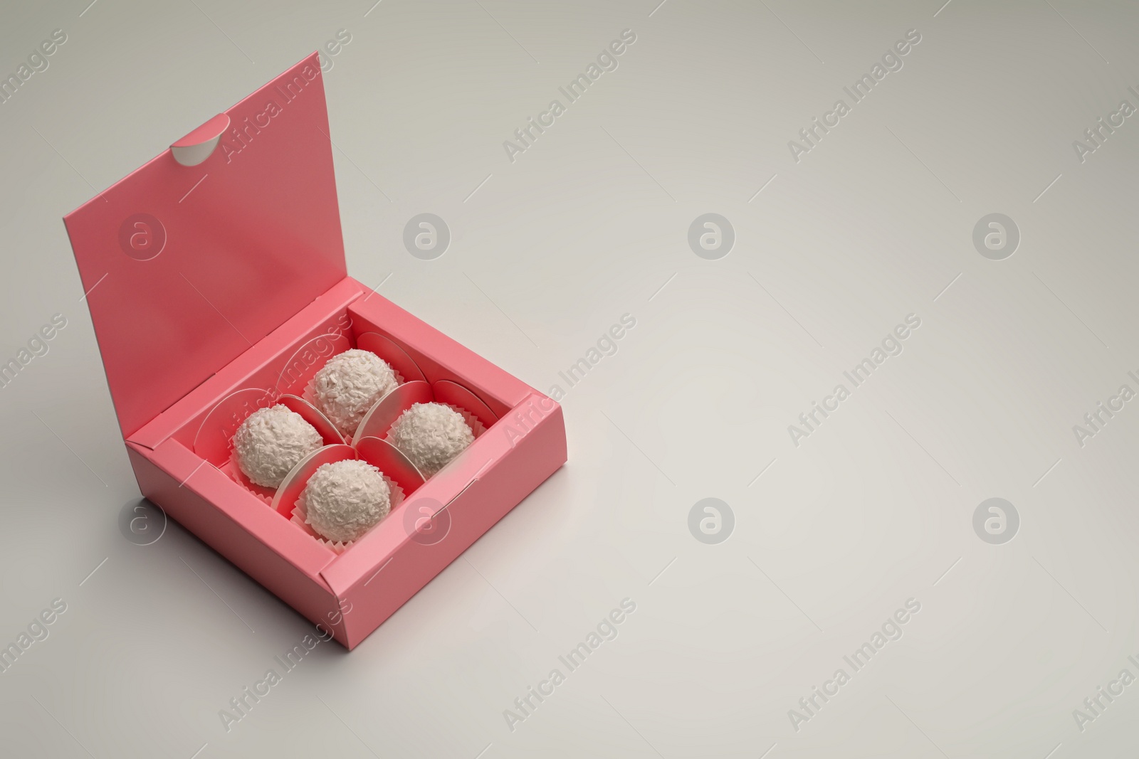 Photo of Delicious candies in pink box on light grey background, space for text