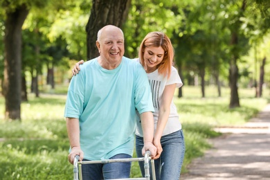 Caretaker helping elderly man with walking frame outdoors