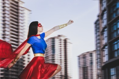 Confident young woman wearing superhero costume and beautiful cityscape on background