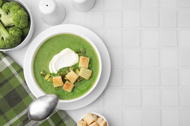Photo of Delicious broccoli cream soup with croutons, sour cream and pumpkin seeds served on white tiled table, flat lay. Space for text