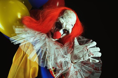 Photo of Terrifying clown with air balloons on black background. Halloween party costume