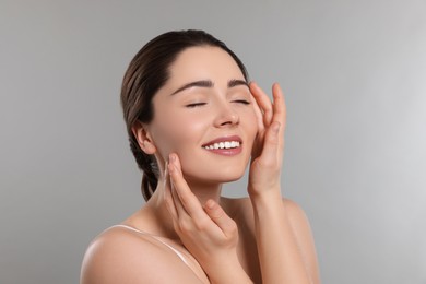 Photo of Young woman massaging her face on grey background