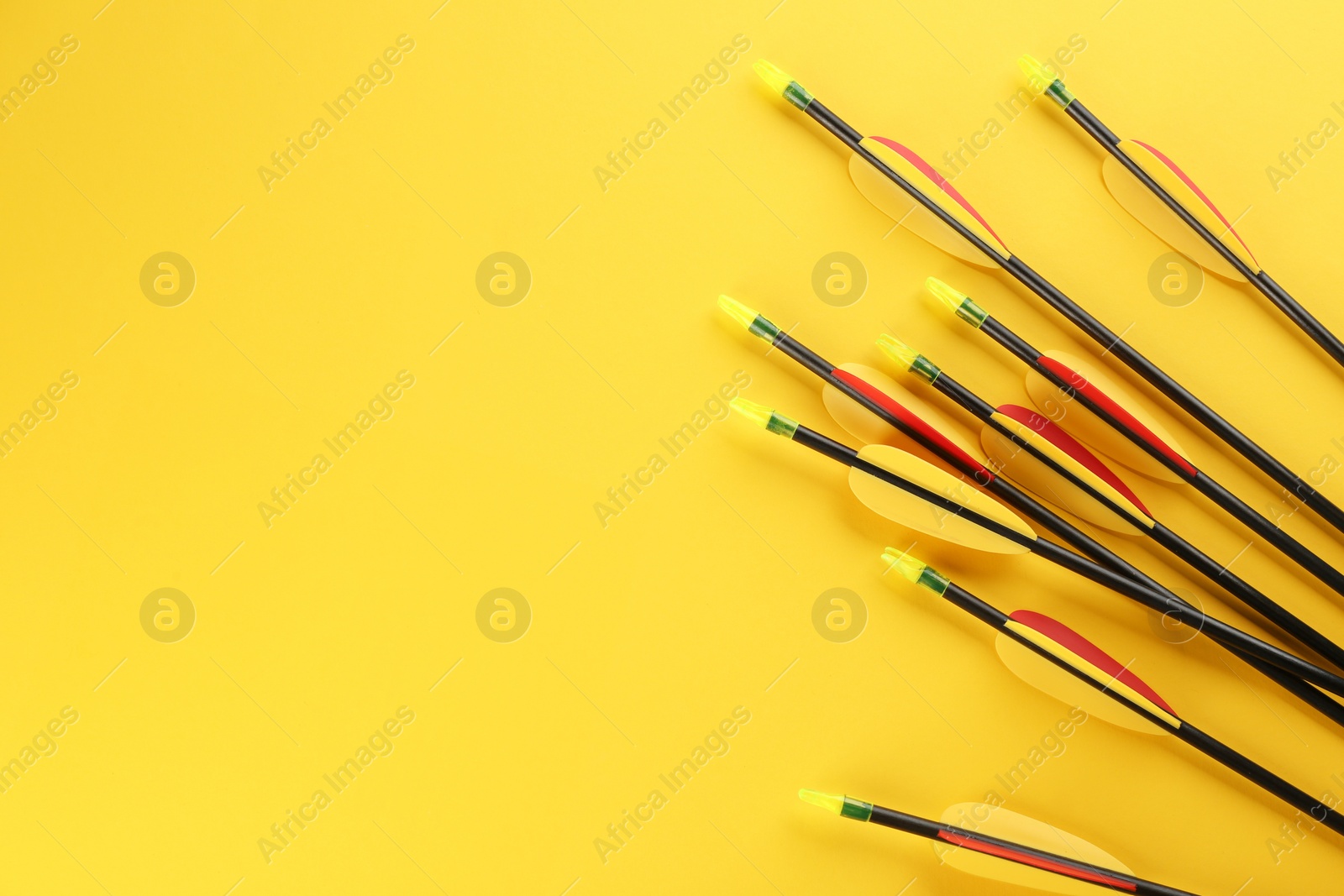 Photo of Many arrows and space for text on yellow background, flat lay. Archery sport equipment