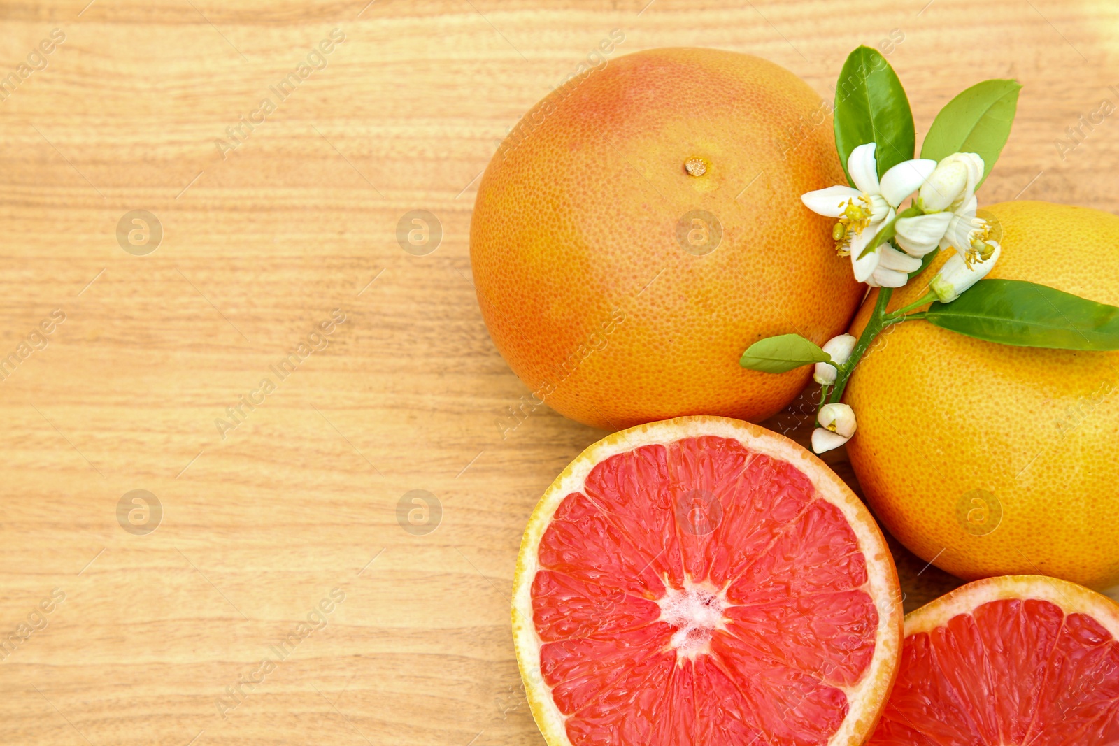 Photo of Fresh ripe grapefruits, flowers and green leaves on wooden table, flat lay. Space for text