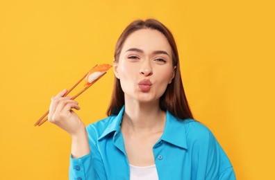 Funny young woman holding sushi with chopsticks on orange background