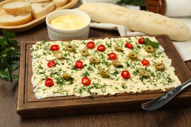 Photo of Fresh natural butter board with cut olives, pepper and knife on wooden table