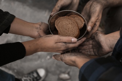 Photo of Poor homeless people with pieces of bread outdoors, closeup
