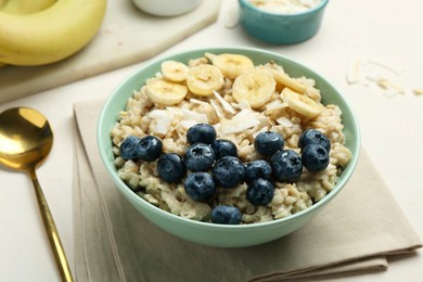 Photo of Tasty oatmeal with banana, blueberries, coconut flakes and honey served in bowl on beige table