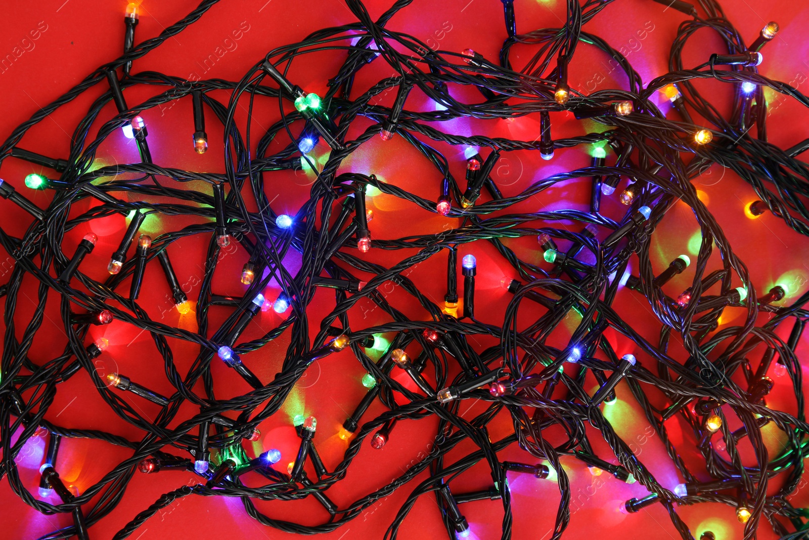 Photo of Glowing Christmas lights on color background, top view