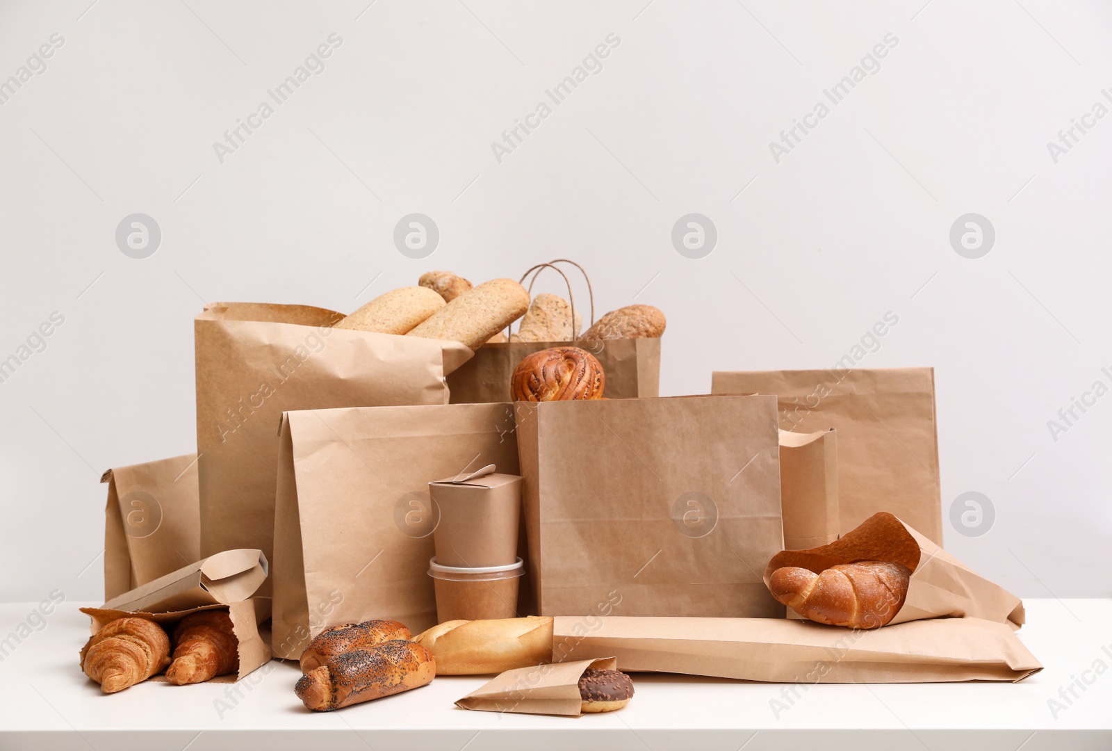 Photo of Different fresh bakery products in paper bags on white background