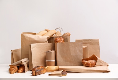 Different fresh bakery products in paper bags on white background