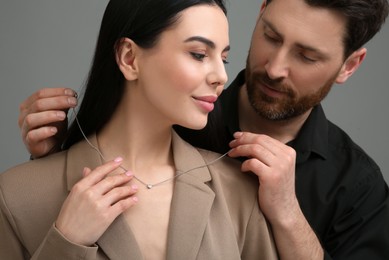 Photo of Man putting elegant necklace on beautiful woman against dark grey background, closeup