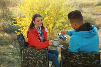 Photo of Couple resting in camping chairs and enjoying hot drink outdoors