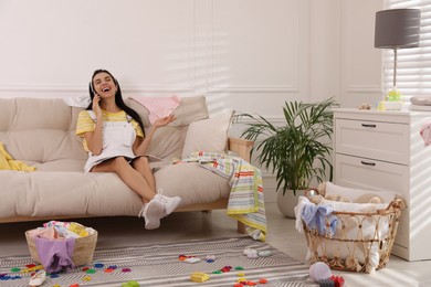 Photo of Young mother with magazine talking by mobile phone on sofa in messy living room