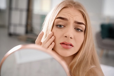 Photo of Young woman with eyelash loss problem looking in mirror indoors