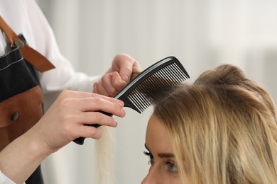 Photo of Hair styling. Professional hairdresser combing woman's hair in salon, closeup