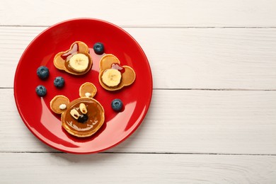 Creative serving for kids. Plate with cute bears made of pancakes, berries, banana and chocolate paste on white wooden table, top view. Space for text