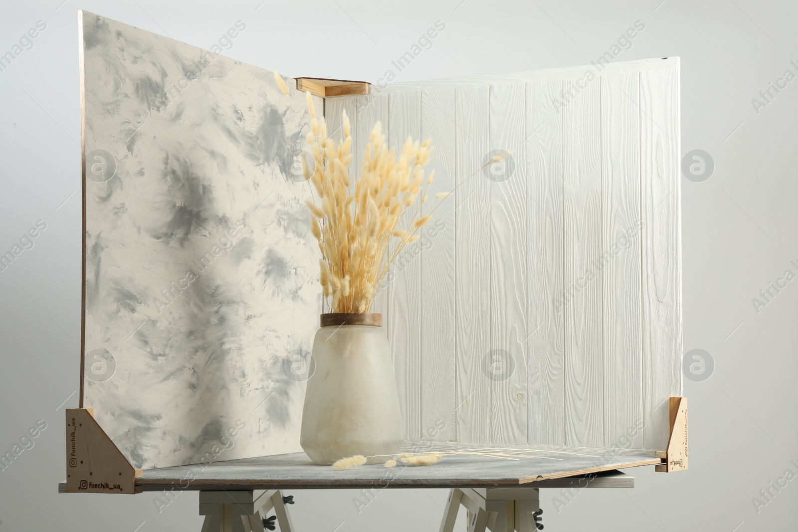Photo of Vase with beautiful dry flowers and double-sided backdrops on table in photo studio