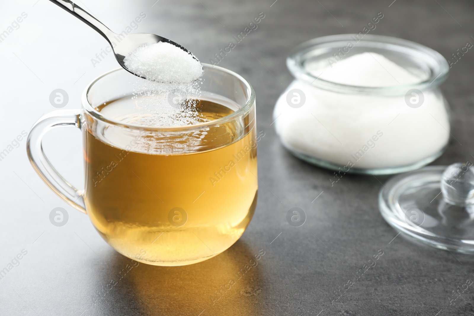 Photo of Adding sugar into aromatic tea at grey table, closeup