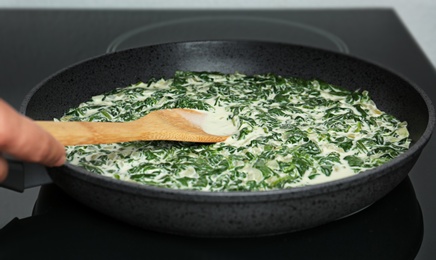 Photo of Woman cooking tasty spinach dip on kitchen stove, closeup view