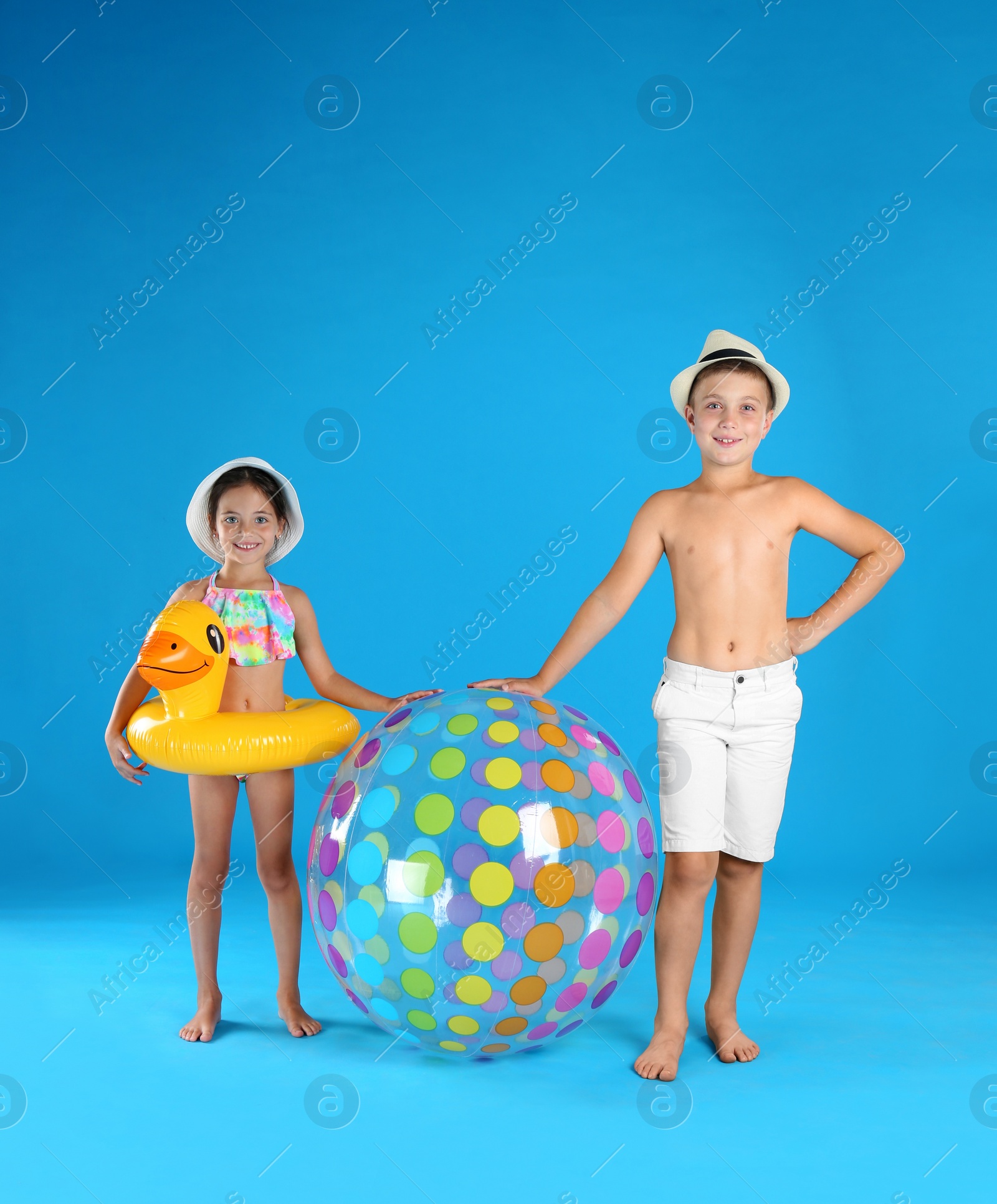 Photo of Cute little children in beachwear with inflatable toys on light blue background