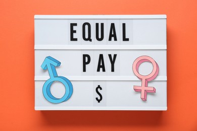 Photo of Equal pay. Lightbox and paper gender symbols on orange background, top view