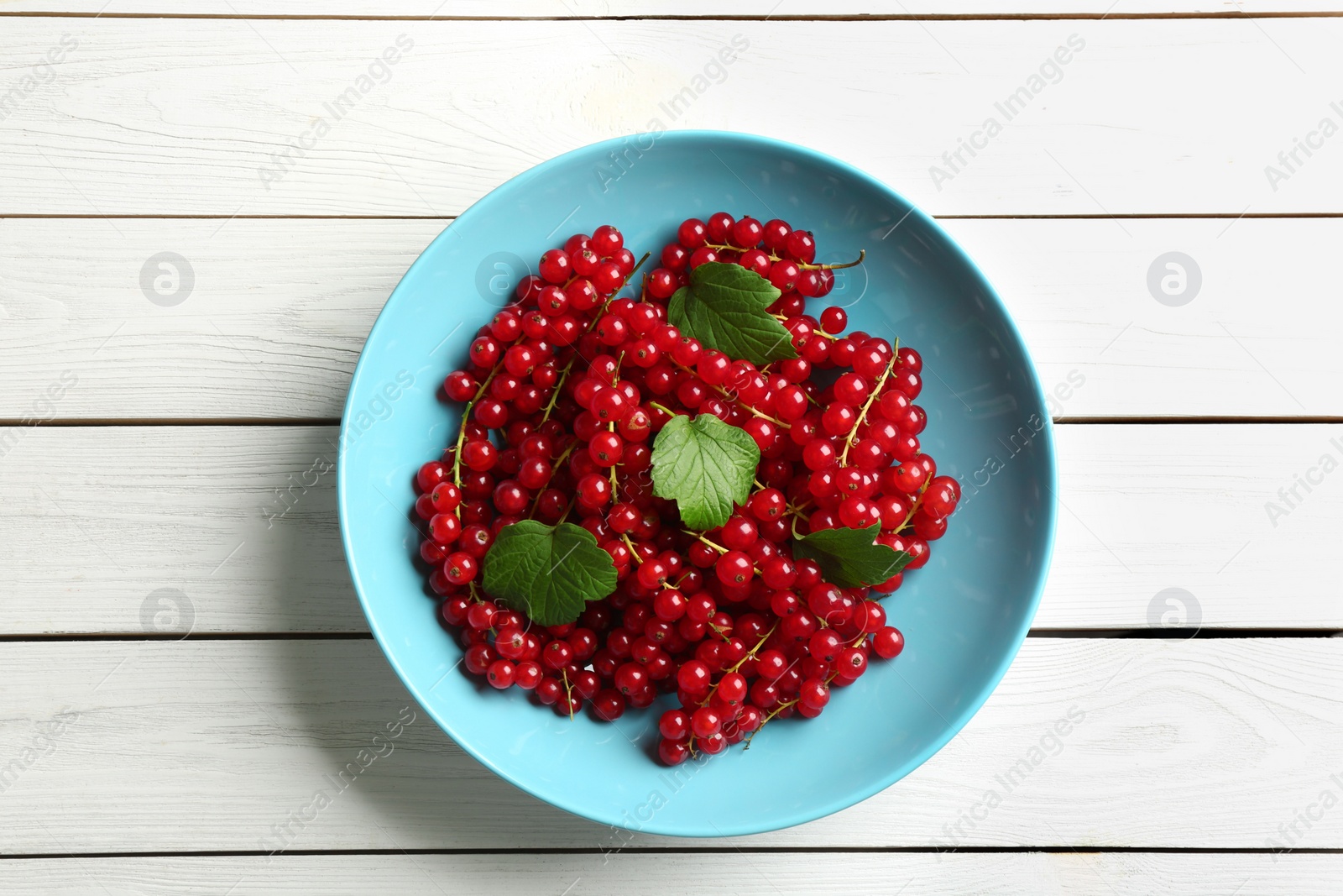 Photo of Delicious red currants and leaves on white wooden table, top view