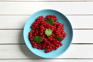 Photo of Delicious red currants and leaves on white wooden table, top view