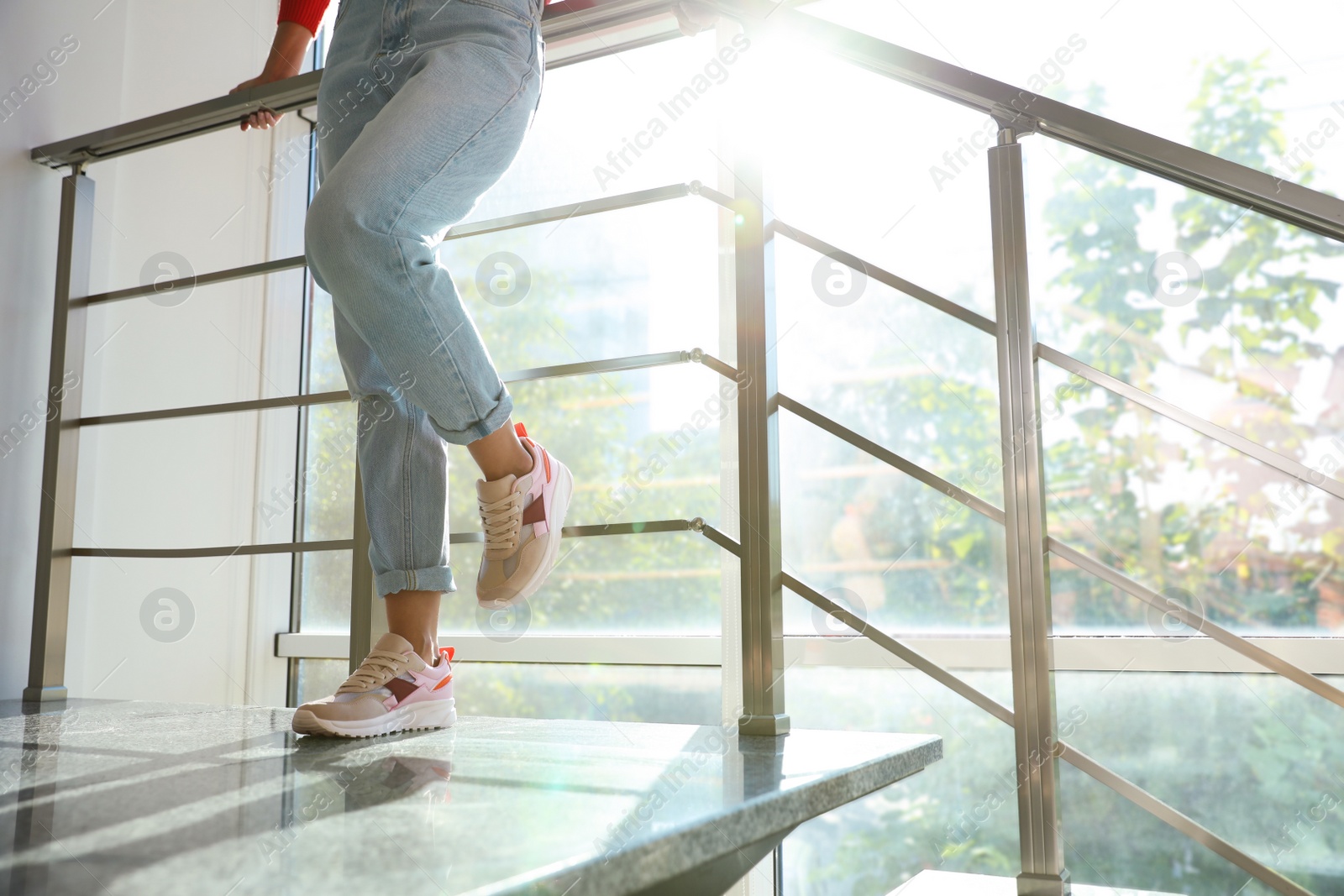 Photo of Young woman wearing stylish sneakers on staircase indoors, closeup