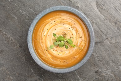 Photo of Delicious pumpkin soup with microgreens in bowl on gray table, top view