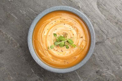 Delicious pumpkin soup with microgreens in bowl on gray table, top view