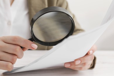 Woman looking at document through magnifier at table, closeup. Searching concept