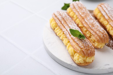 Photo of Delicious eclairs filled with cream and mint on white tiled table, space for text