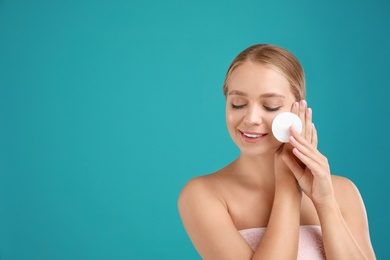 Photo of Beautiful young woman with cotton pad on turquoise background. Space for text