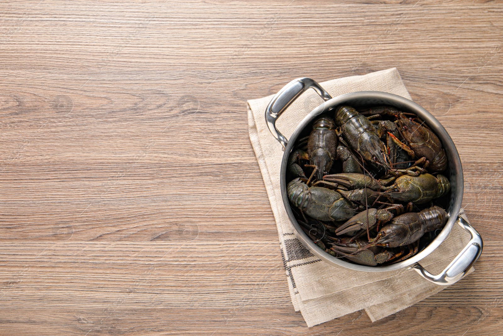 Photo of Fresh raw crayfishes in pot on wooden table, top view. Space for text
