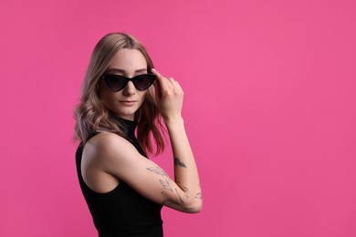 Photo of Beautiful woman with tattoos on arm against pink background. Space for text