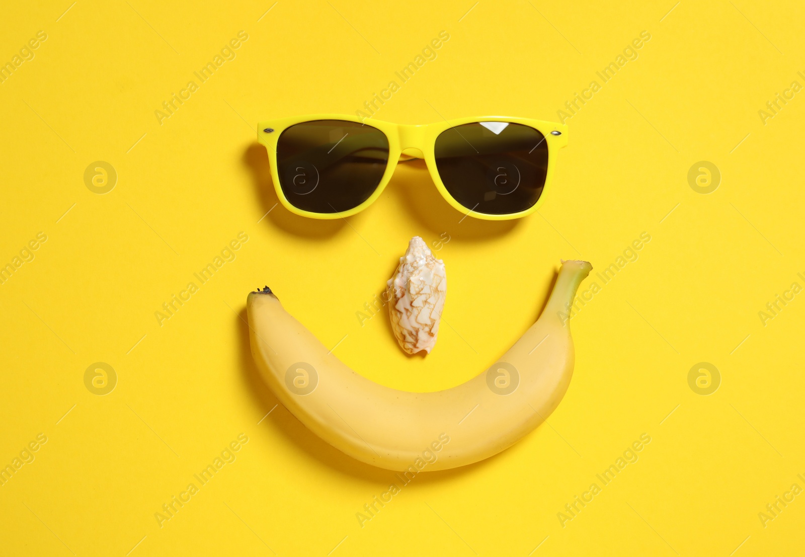 Photo of Funny face of sunglasses, banana and seashell on color background, top view. Beach accessories