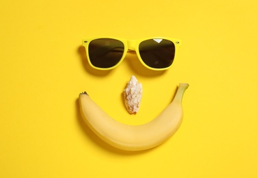 Photo of Funny face of sunglasses, banana and seashell on color background, top view. Beach accessories