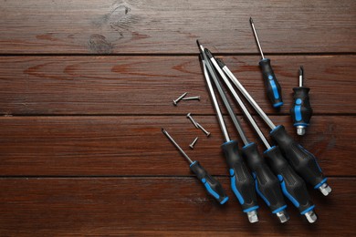 Photo of Set of screwdrivers and screws on wooden table, flat lay. Space for text