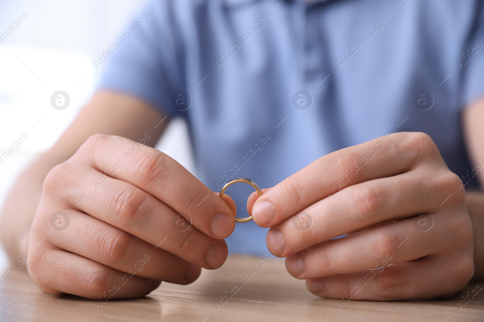 Photo of Man holding wedding ring at wooden table, closeup. Divorce concept