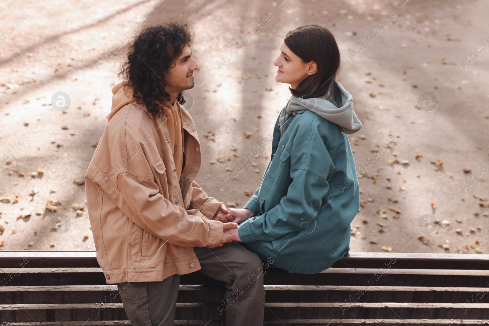 Photo of Young couple spending time together on wooden bench outdoors. Dating agency