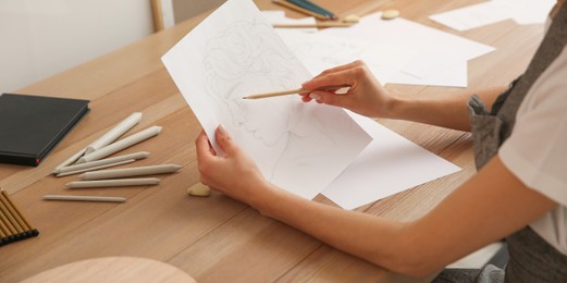 Image of Young woman drawing male portrait at table indoors, closeup. Banner design