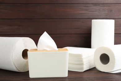 Photo of Clean napkins, box with tissues and rolls of paper towels on wooden table