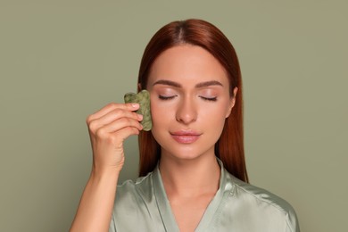 Photo of Young woman massaging her face with jade gua sha tool on green background