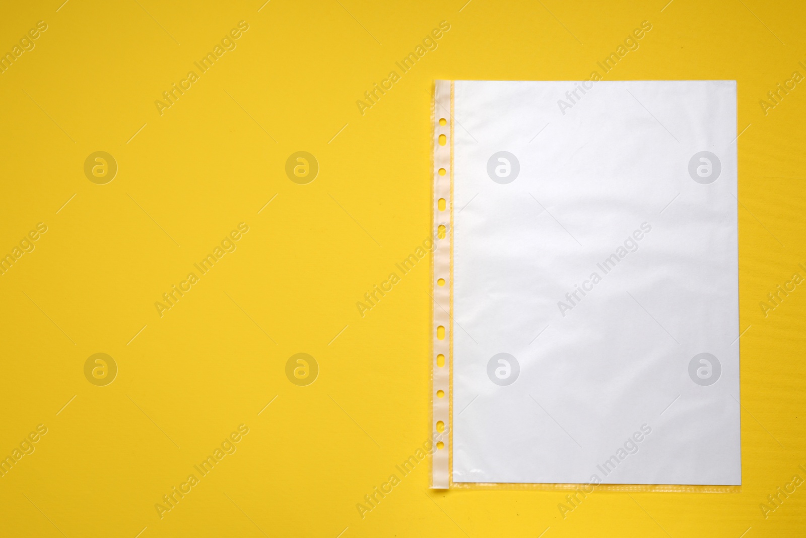 Photo of Punched pocket with paper sheet on yellow background, top view. Space for text