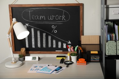 Photo of Business process planning and optimization. Workplace with lamp, blackboard, graphs and other stationery on wooden table