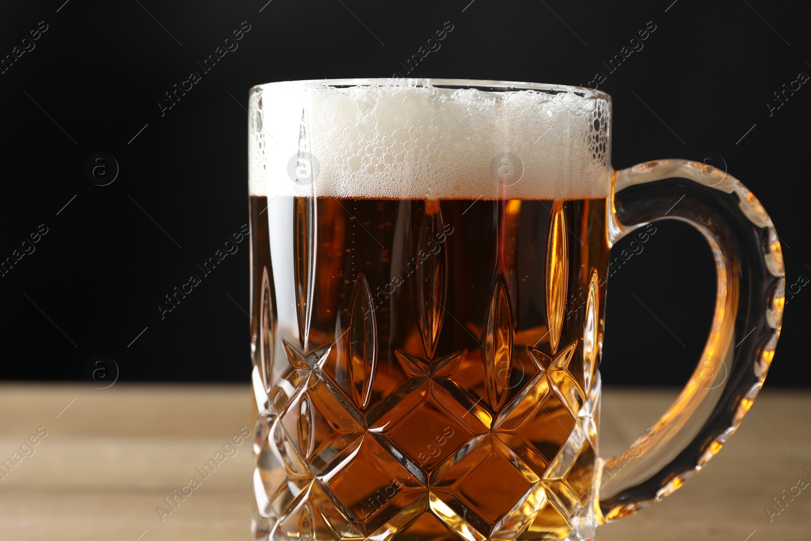 Photo of Mug with fresh beer on table against black background, closeup