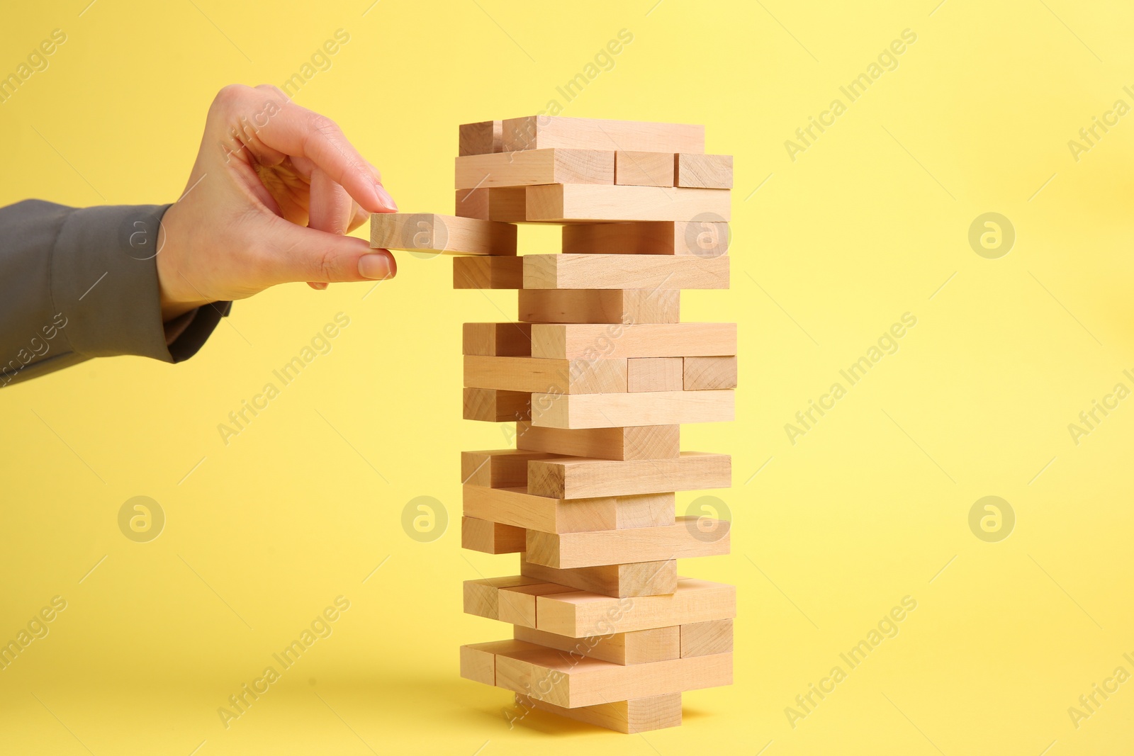 Photo of Woman playing Jenga tower on yellow background, closeup